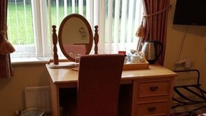A wooden desk with a chair, a mirror, a radiator, and a window with curtains. - Nyton Hotel (Ely)
