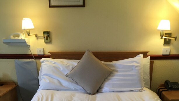 A neatly made bed with white linens and a single gray pillow, flanked by two bedside tables with lamps, in a hotel room. - Nyton Hotel (Ely)