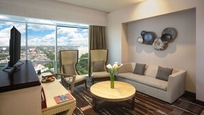 A modern hotel room with a large window offering a city view, a comfortable sofa, a small round table, and a TV on a stand. - Swiss-Belresidences Kalibata Jakarta (Jakarta)