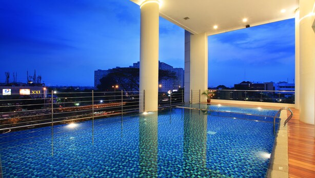 An indoor swimming pool with clear blue tiles, surrounded by white pillars and a wooden deck. - Swiss-Belresidences Kalibata Jakarta (Jakarta)