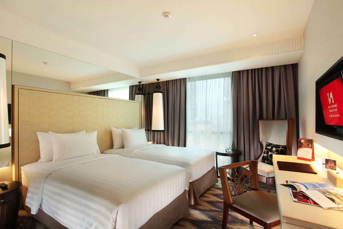 A hotel room with two beds, a desk, a chair, a television, and a large mirror.