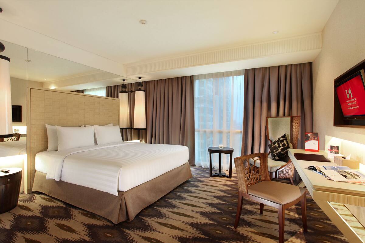 A hotel room with a large bed, a desk with a chair, a small table, and a TV on the wall.