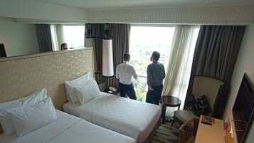A hotel room with two beds, a desk, a chair, and a large window with curtains.