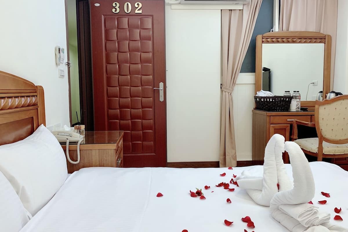 A hotel room with a bed, a desk, a chair, a mirror, a door with the number 302, and a telephone.