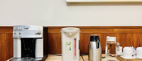 Una cafetera, un hervidor de agua y un termo sobre una mesa de madera en una habitación con panel de madera y un cuadro enmarcado en la pared.