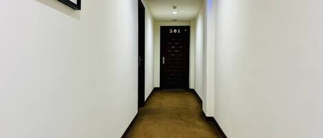 A narrow, carpeted hallway with white walls, a framed picture on the left, and a door marked '501' at the end.