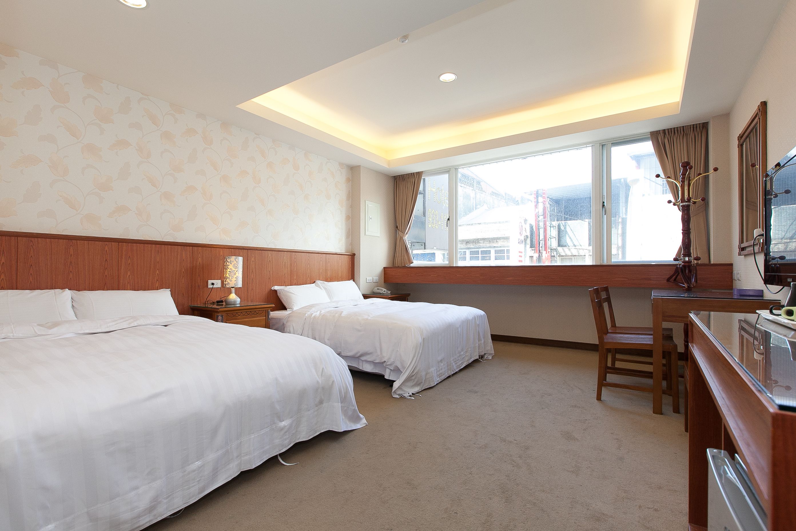 A hotel room with two beds, a desk, a chair, a TV, and a window with a view of mountains.