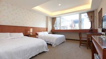 A hotel room with two beds, a desk, a chair, a TV, and a window with a view of mountains.
