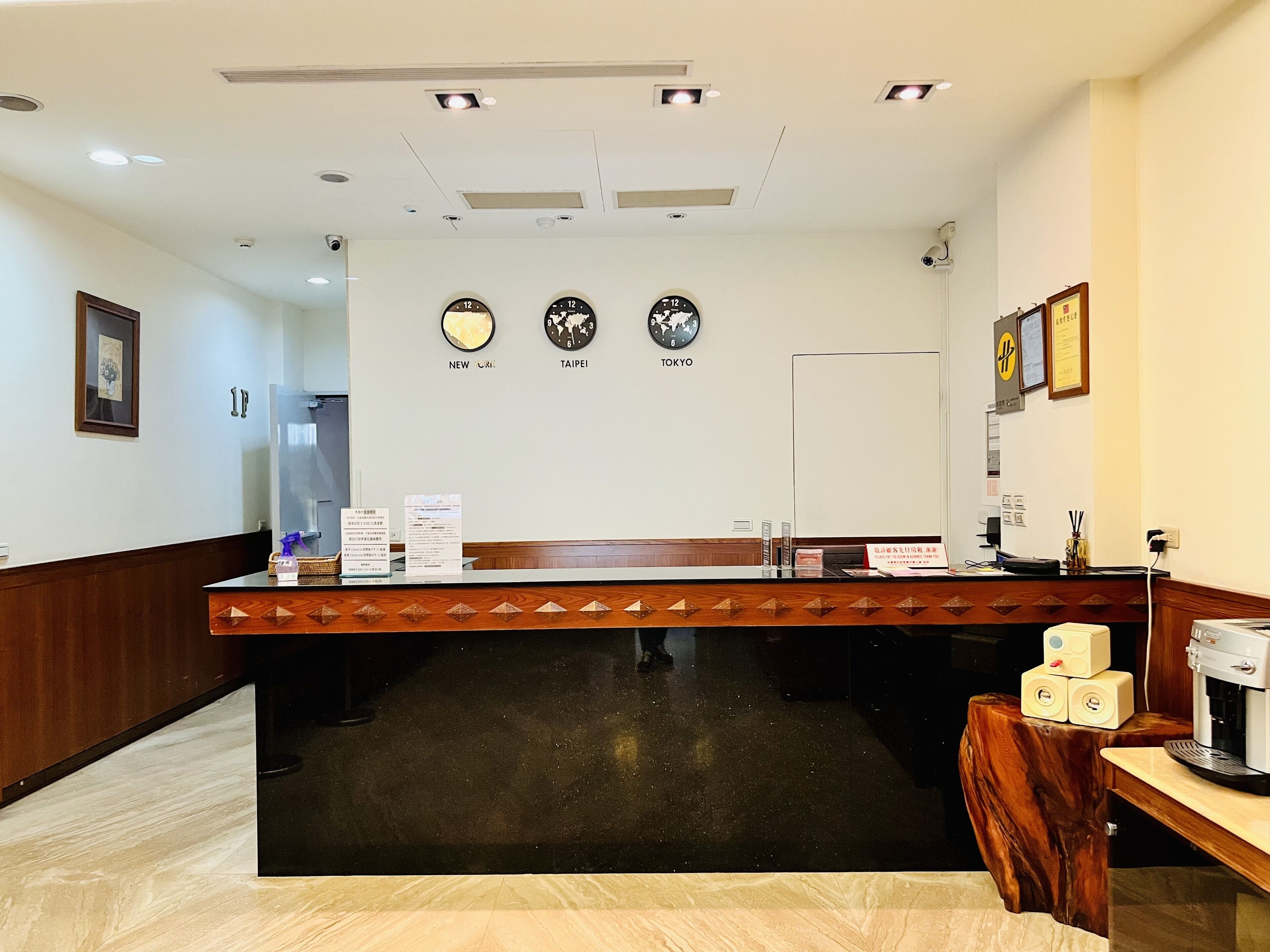Un área de recepción con un mostrador de madera, una máquina de café y relojes que muestran la hora de Nueva York, Taipéi y Tokio.