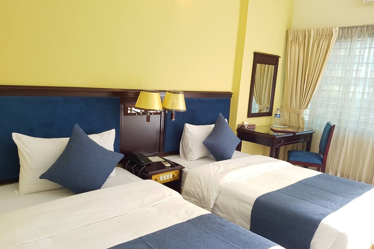 A hotel room with two beds, a desk, a chair, a telephone, and a mirror.