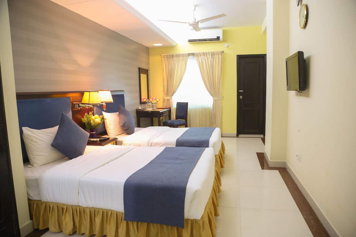 A hotel room with two beds, a desk, a chair, a TV, and a door.