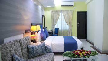 Habitación de hotel con cama, sofá, una mesa de centro de vidrio con flores, lámpara y televisor.