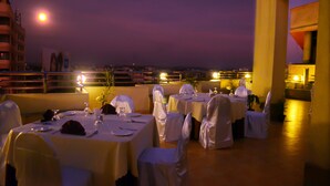A rooftop dining area with tables set for a meal, under a night sky with a visible moon. - Hotel Valley Garden (Sylhet)