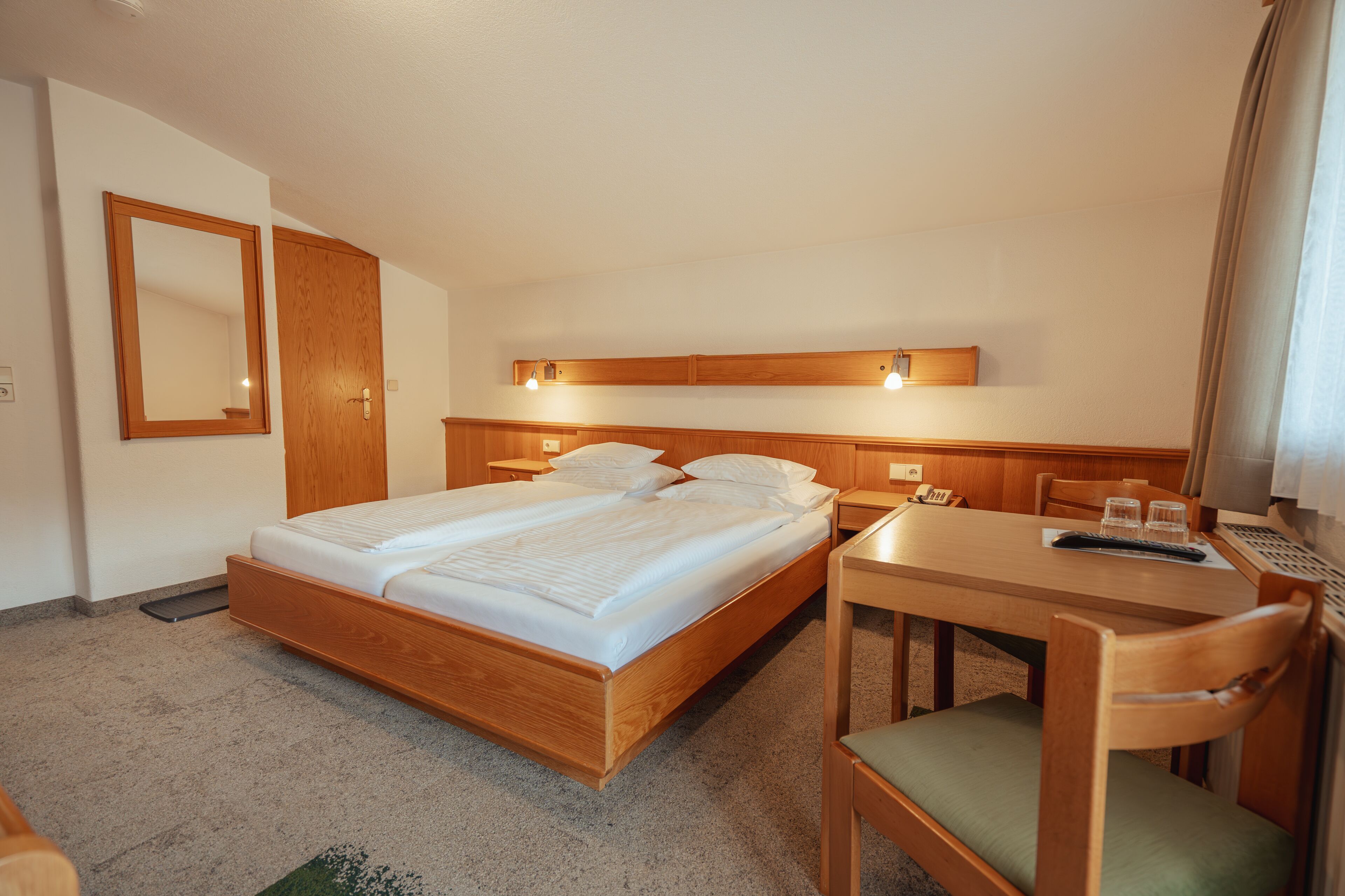Una habitación de hotel con una cama de madera, un escritorio con una silla y un espejo en la pared.