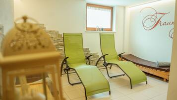 A room with two green lounge chairs, a wooden bench, and a stone wall.