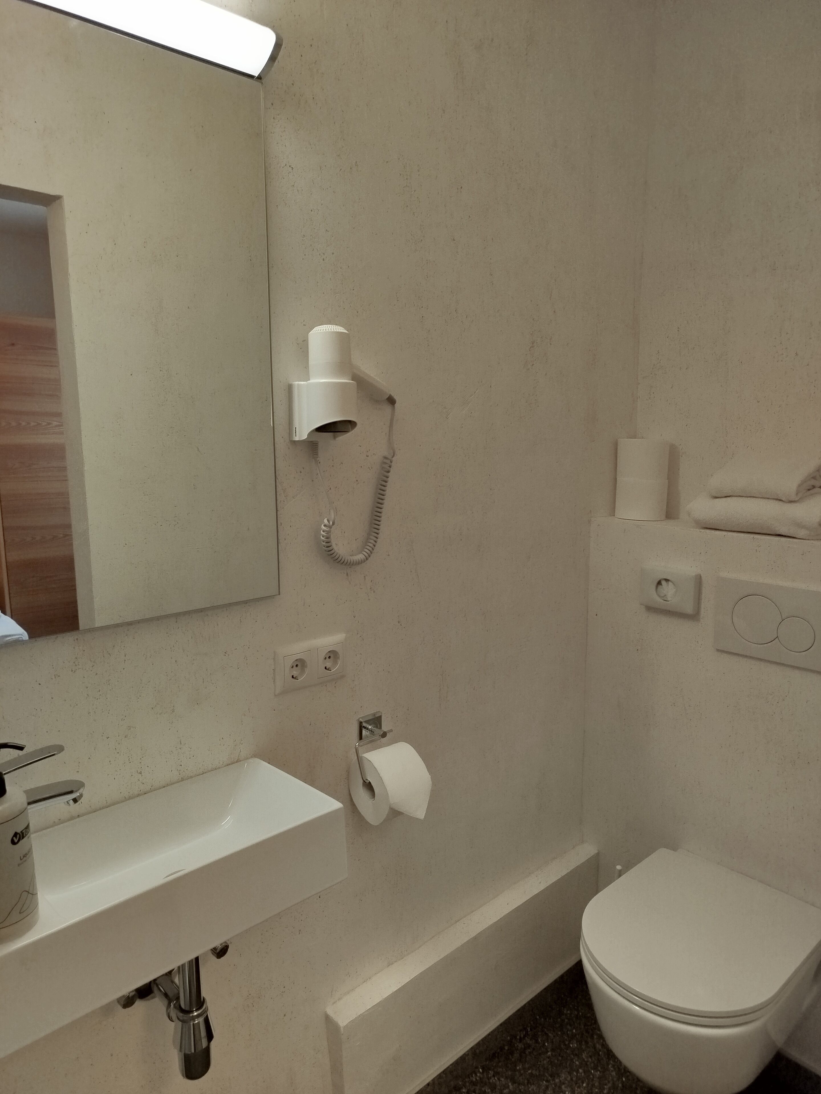 Un baño con lavamanos, inodoro y secador de pelo montado en la pared.
