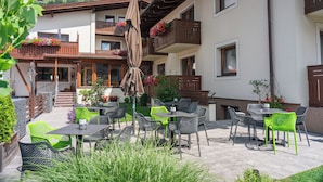 Une terrasse extérieure avec des tables et des chaises, un espace salon abrité et des jardinières sur les balcons.