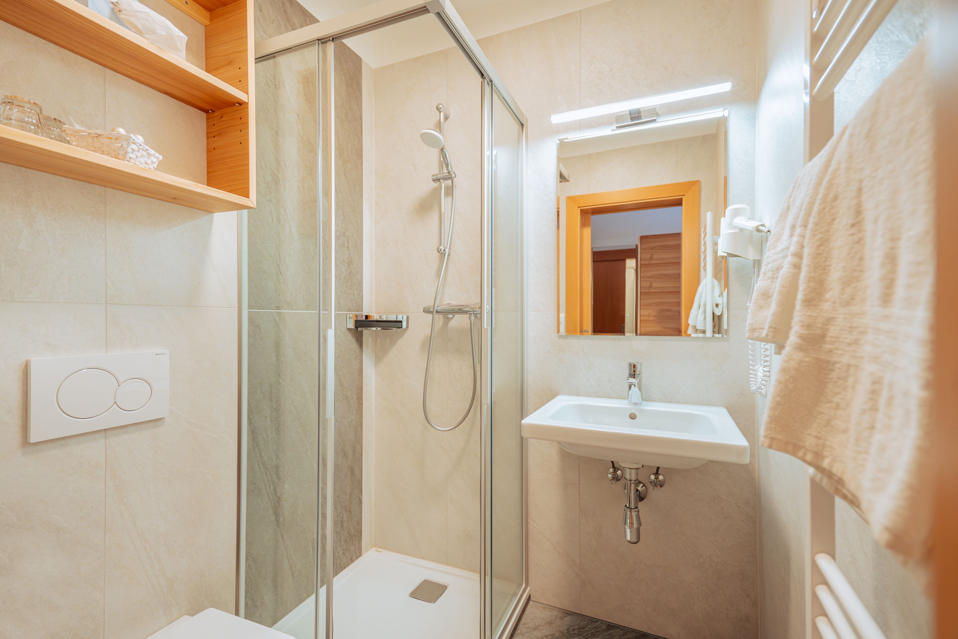 Un bagno moderno con doccia vetrata, lavandino bianco e mensole in legno.