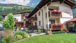 Un hôtel doté d’un balcon orné de fleurs, d’un patio avec des sièges en plein air et offrant une vue sur un paysage montagneux.