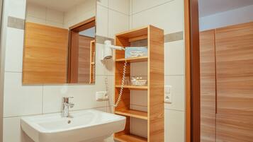 Une salle de bain avec un lavabo blanc, des étagères en bois, un miroir et un sèche-cheveux.