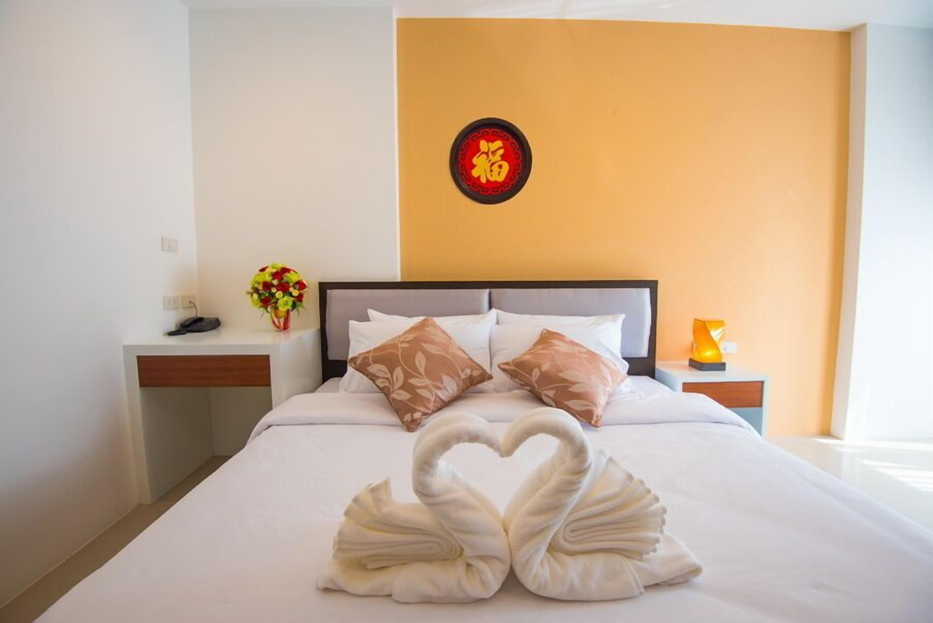 Una habitación de hotel con cama, mesita de noche, decoración en la pared y un jarrón de flores.