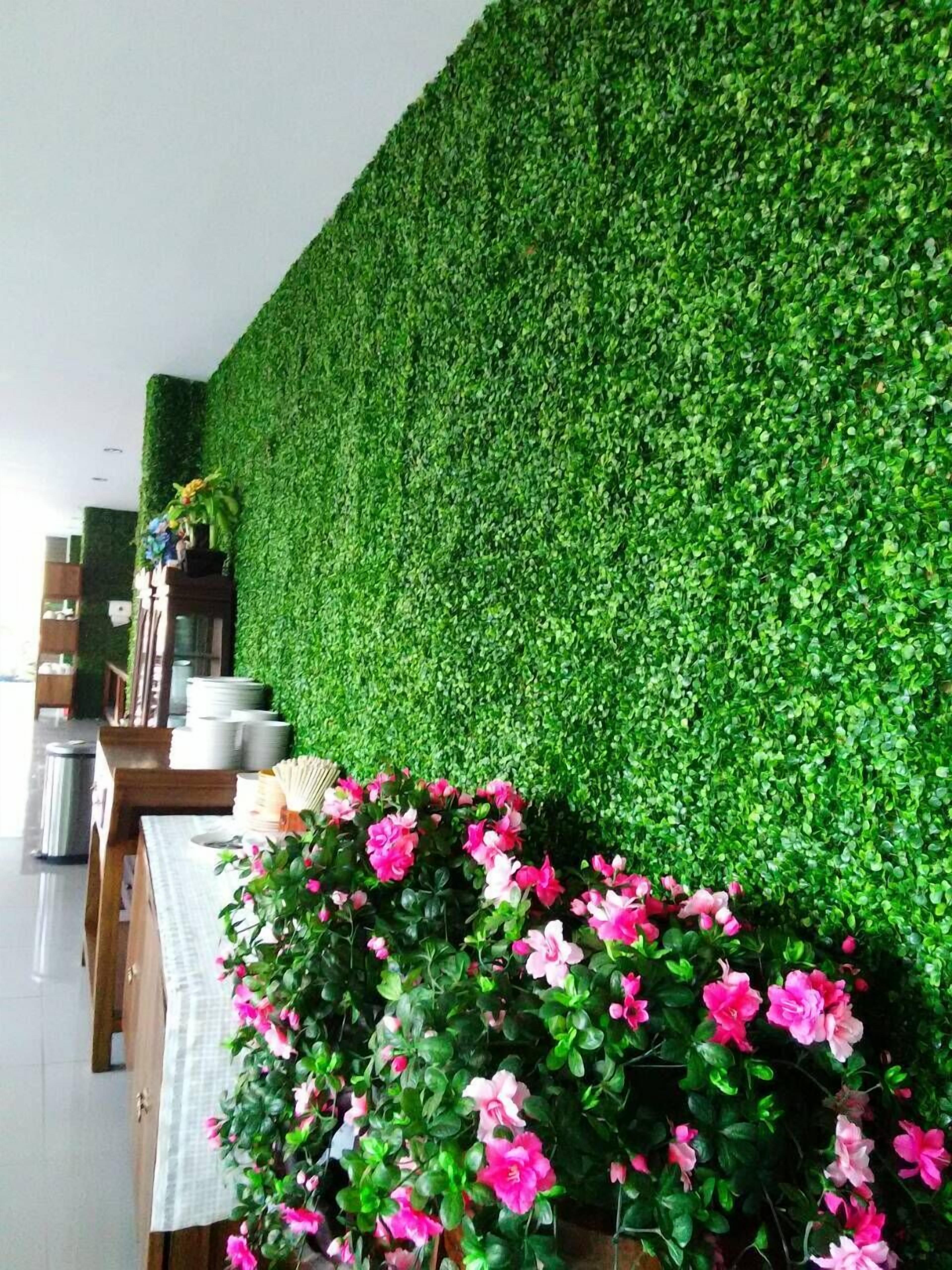 Een kamer met een groene wand begroeid met planten, een tafel met een witte tafelkleed, en roze bloemen in een vaas.
