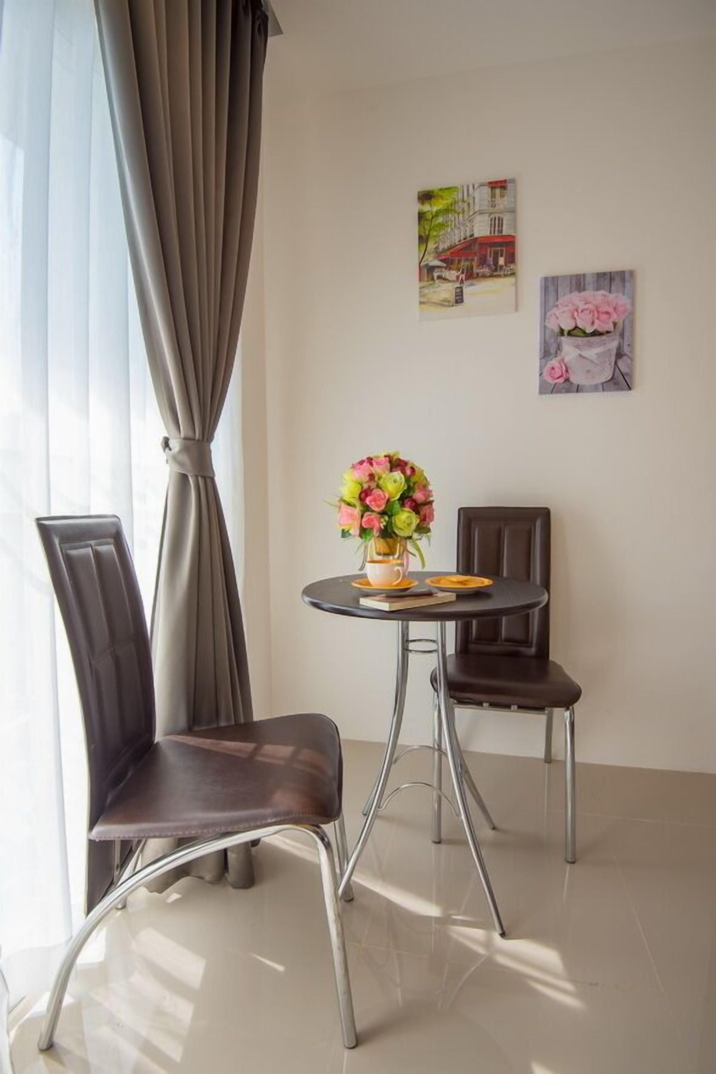 A room with two chairs, a small table with a vase of flowers, and two paintings on the wall.