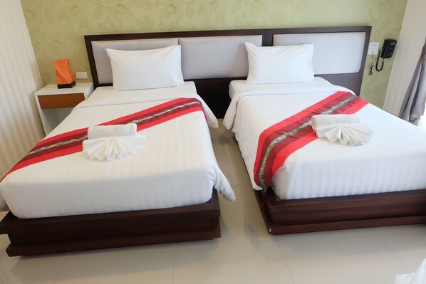 Habitación de hotel con dos camas, cada una con ropa blanca y detalles decorativos rojos. Se ve una mesita de noche con un teléfono y un objeto naranja.
