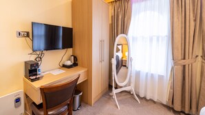 Une chambre d’hôtel avec un bureau en bois, une télévision, un miroir et une fenêtre avec des rideaux.