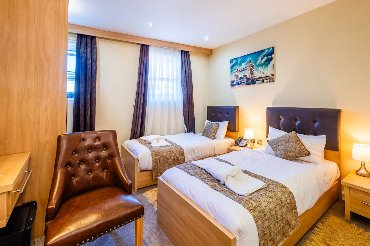 Quarto de hotel com duas camas, uma poltrona de couro marrom, uma escrivaninha e um quadro de uma ponte.