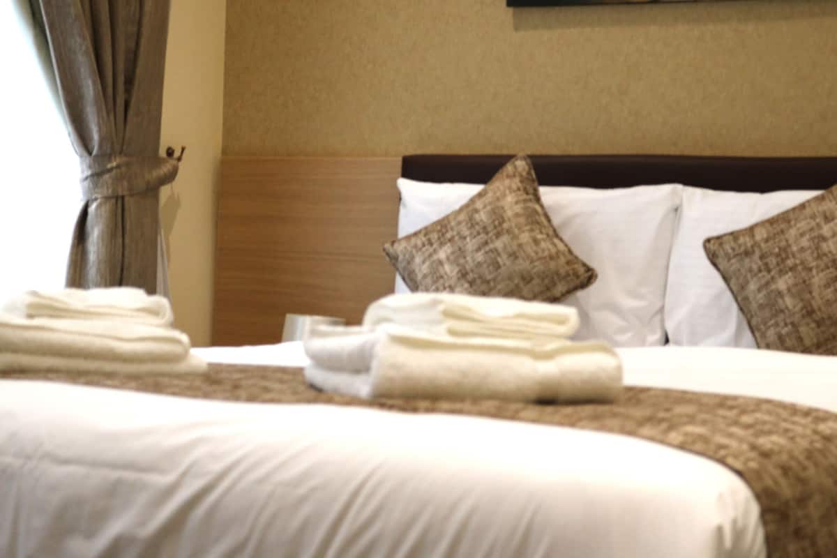 Cama bem arrumada com lençóis brancos e castanhos, dois travesseiros e uma toalha dobrada ao lado.