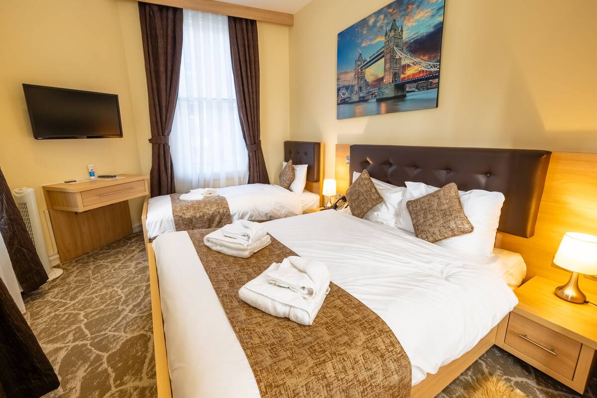Quarto de hotel com duas camas, uma TV de tela plana, um quadro de uma ponte e piso coberto de carpete.