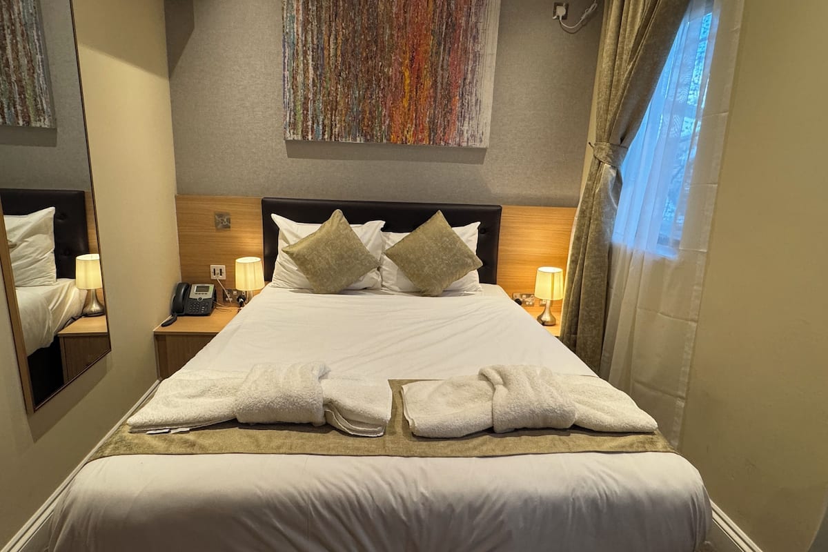 Quarto de hotel com uma cama grande, duas luminárias de cabeceira, um telefone e um espelho em uma das laterais.