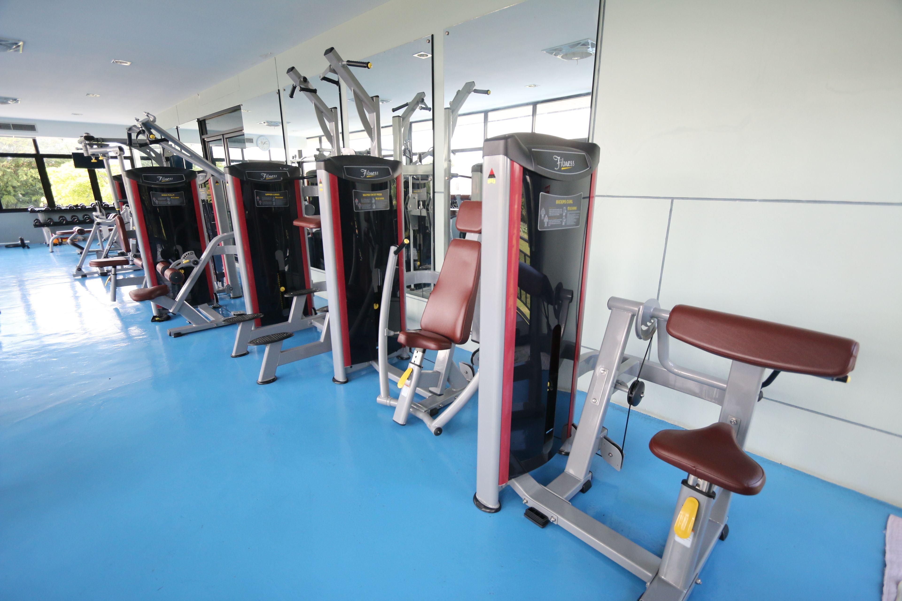 A gym with various exercise machines, a blue floor, and large windows.