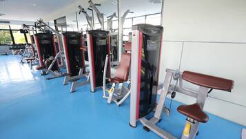 A gym with various exercise machines, a blue floor, and large windows.