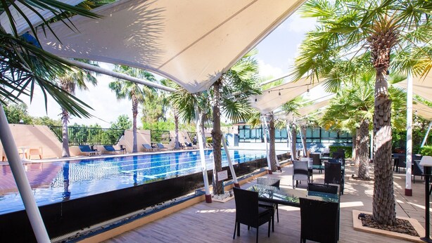 An outdoor pool area with a wooden deck, lounge chairs, and palm trees. - Ray Hotel (Buriram)