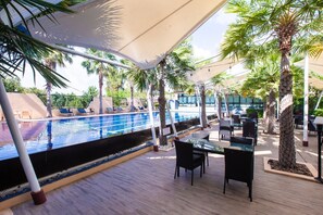 An outdoor pool area with a wooden deck, lounge chairs, and palm trees. - Ray Hotel (Buriram)