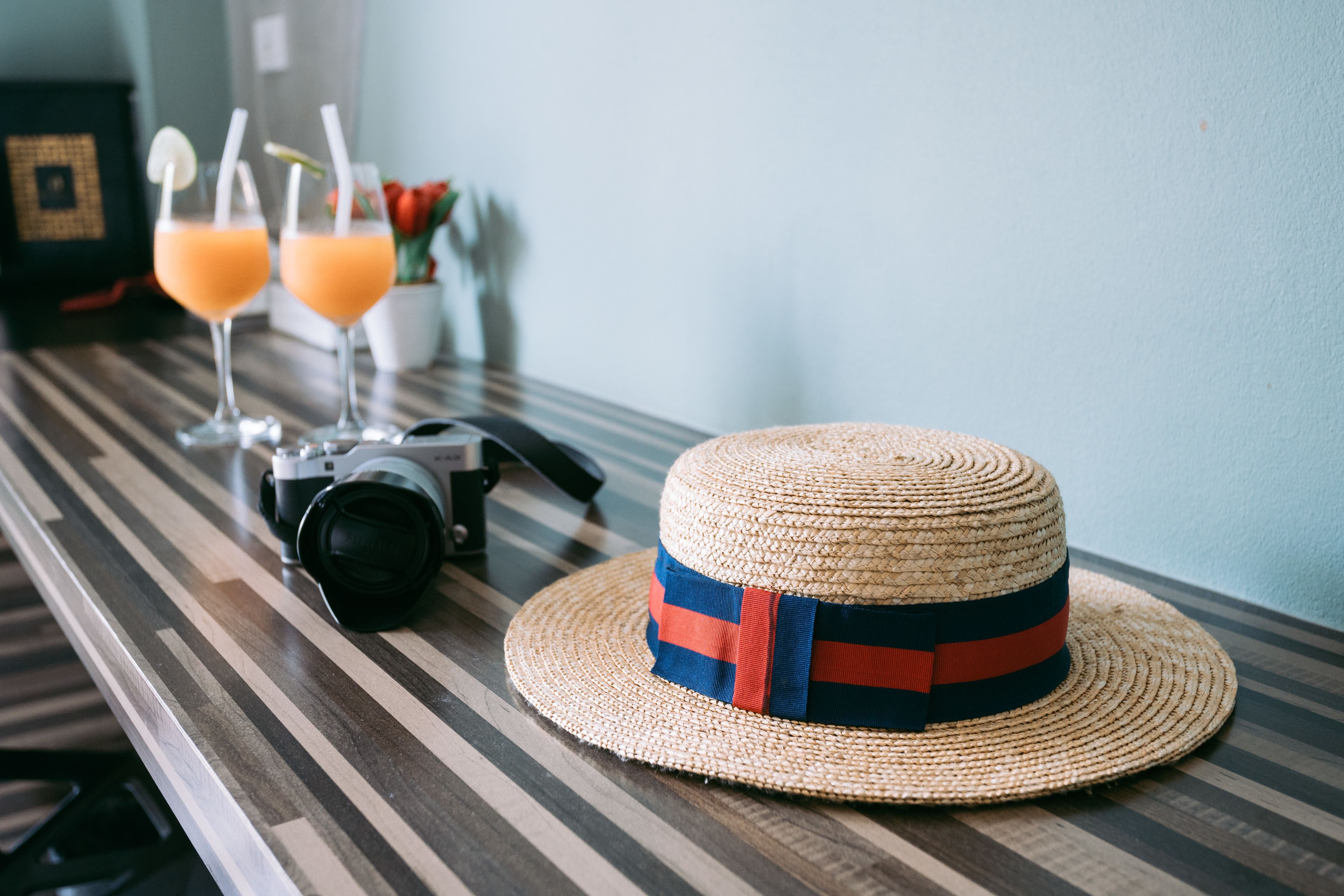 Un sombrero de paja con una cinta azul y roja sobre una mesa de madera a rayas.