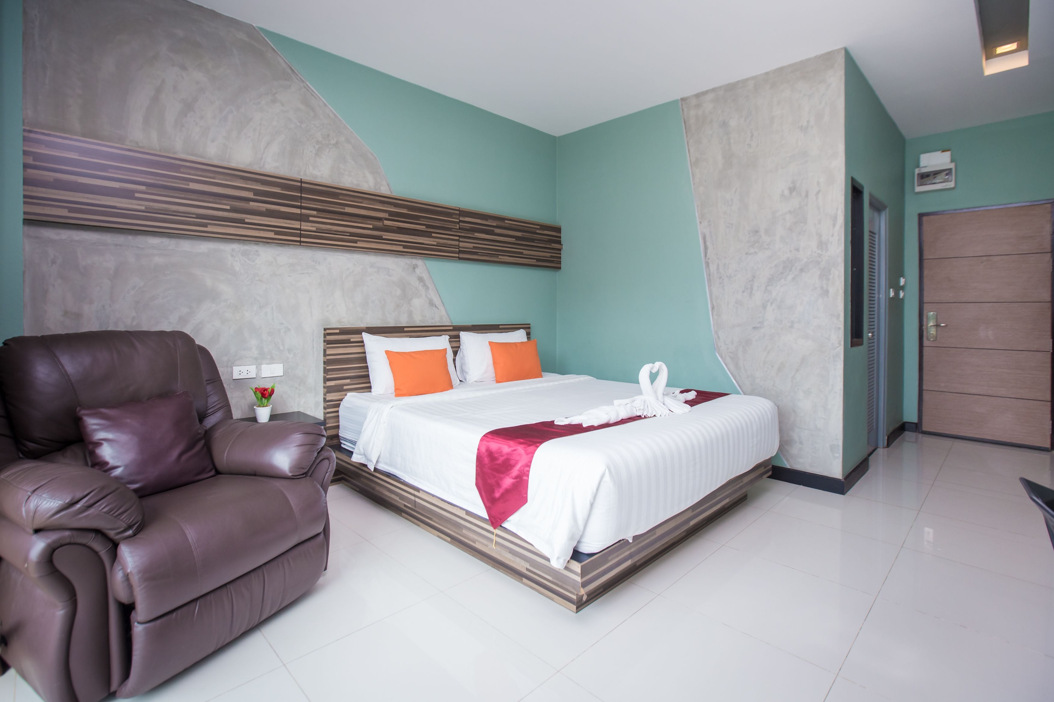 A modern hotel room with a large bed, a leather sofa, and a marble accent wall.