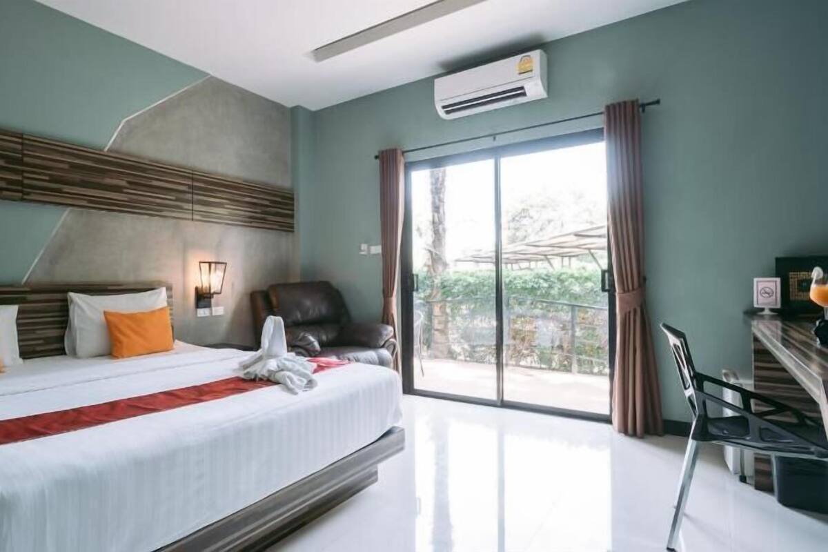Une chambre d’hôtel avec un grand lit, une chaise, un bureau et une vue sur la verdure.