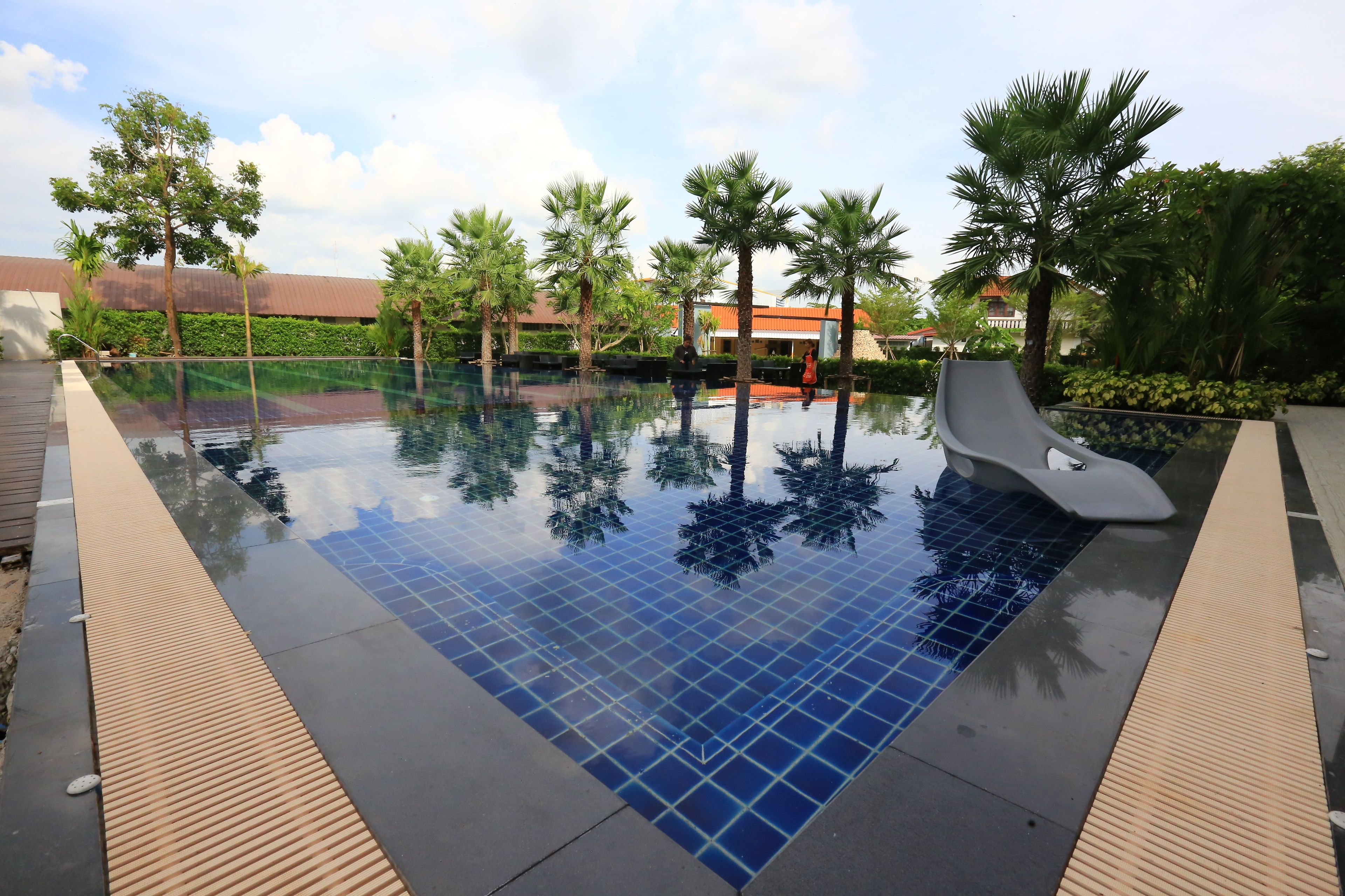 Ein Pool mit Fliesenboden und Rutsche, umgeben von Palmen und einem Gebäude im Hintergrund.