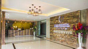 A hotel reception area with a modern design, featuring a reception desk, a chandelier, and a stone wall with the hotel's name. - Ray Hotel (Buriram)