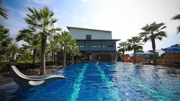 A swimming pool with a modern design, surrounded by palm trees and a building with a flat roof.