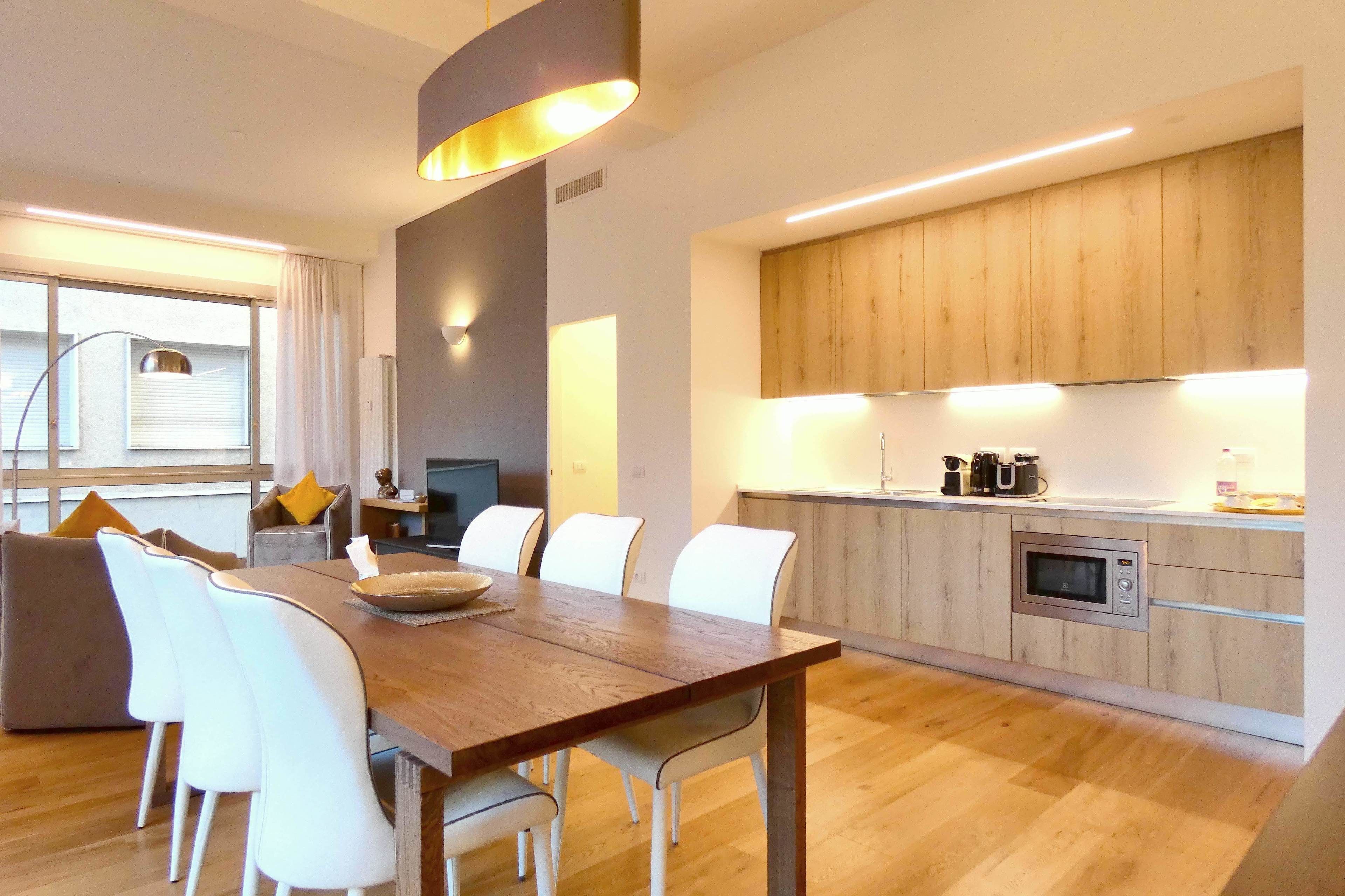 Une cuisine moderne avec des meubles en bois, un four à micro-ondes encastré et un coin repas comprenant une table en bois et des chaises blanches.