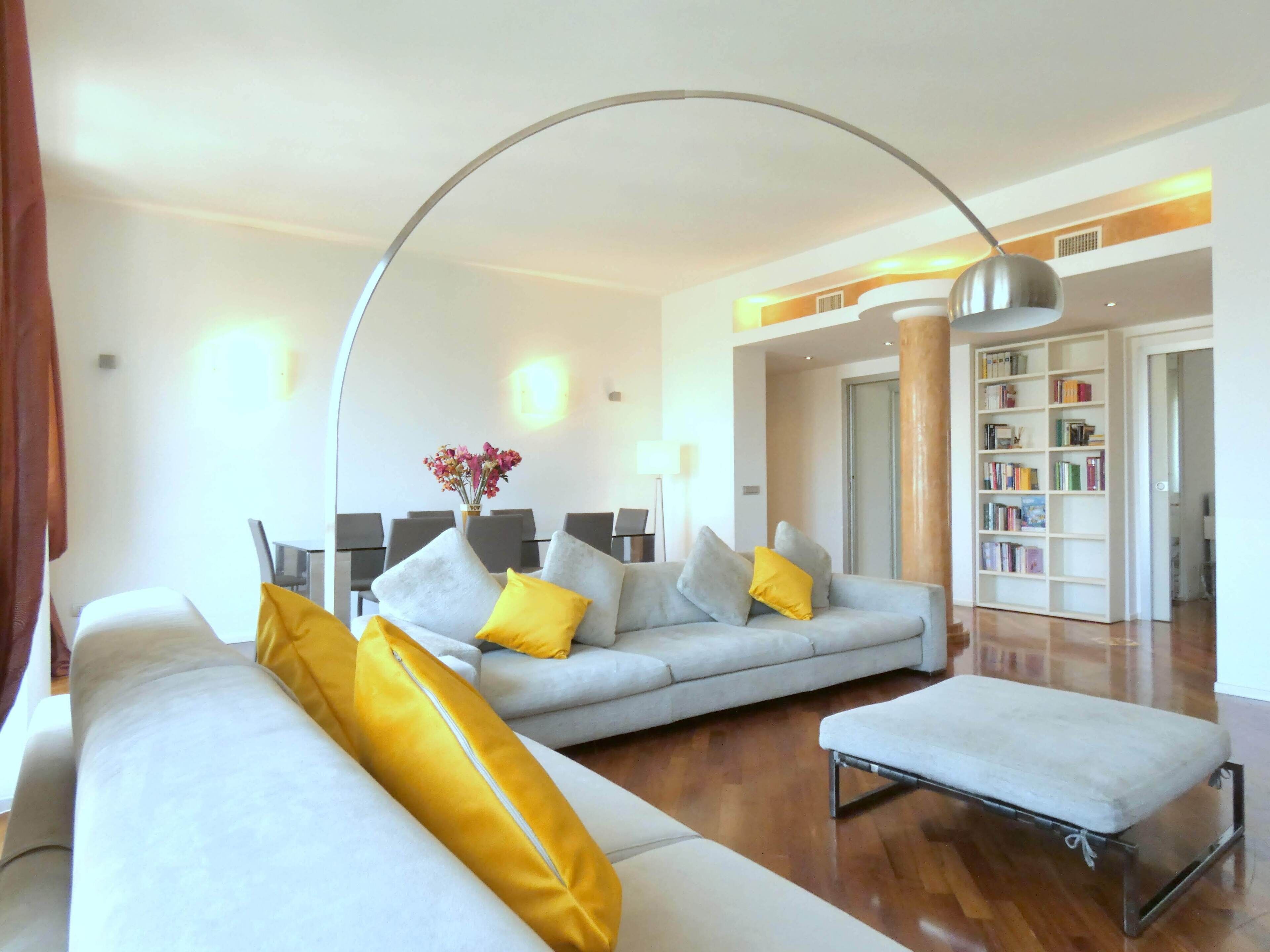 A modern living room with a grey sofa, yellow cushions, a coffee table, and a bookshelf.