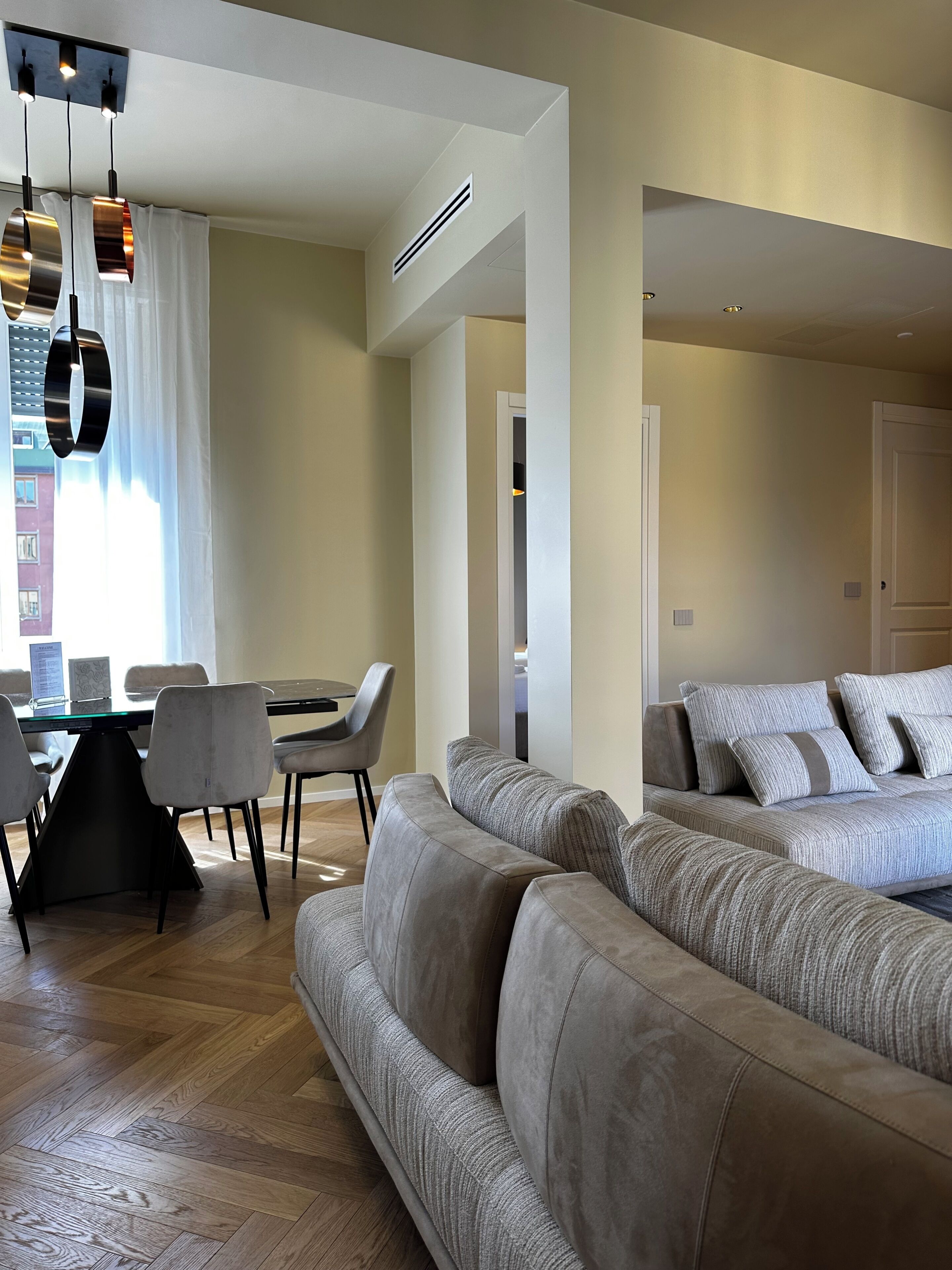 A modern living room with a sofa set, dining area, and pendant lighting.