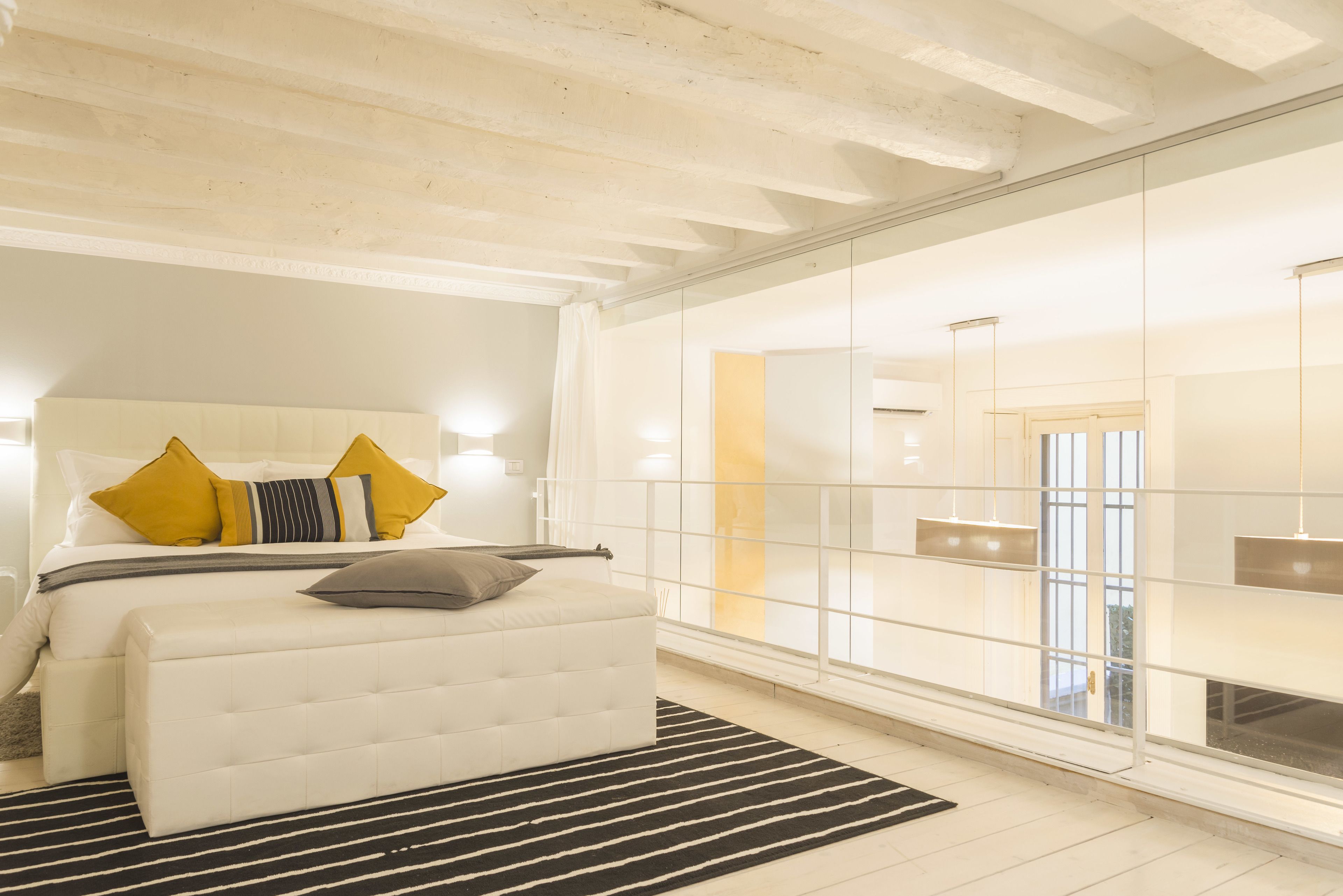 A modern bedroom with a large bed, a white headboard, and a large window with a view.