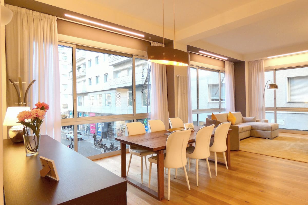 Una sala de estar moderna con una mesa de comedor de madera, sillas blancas y un sofá gris.