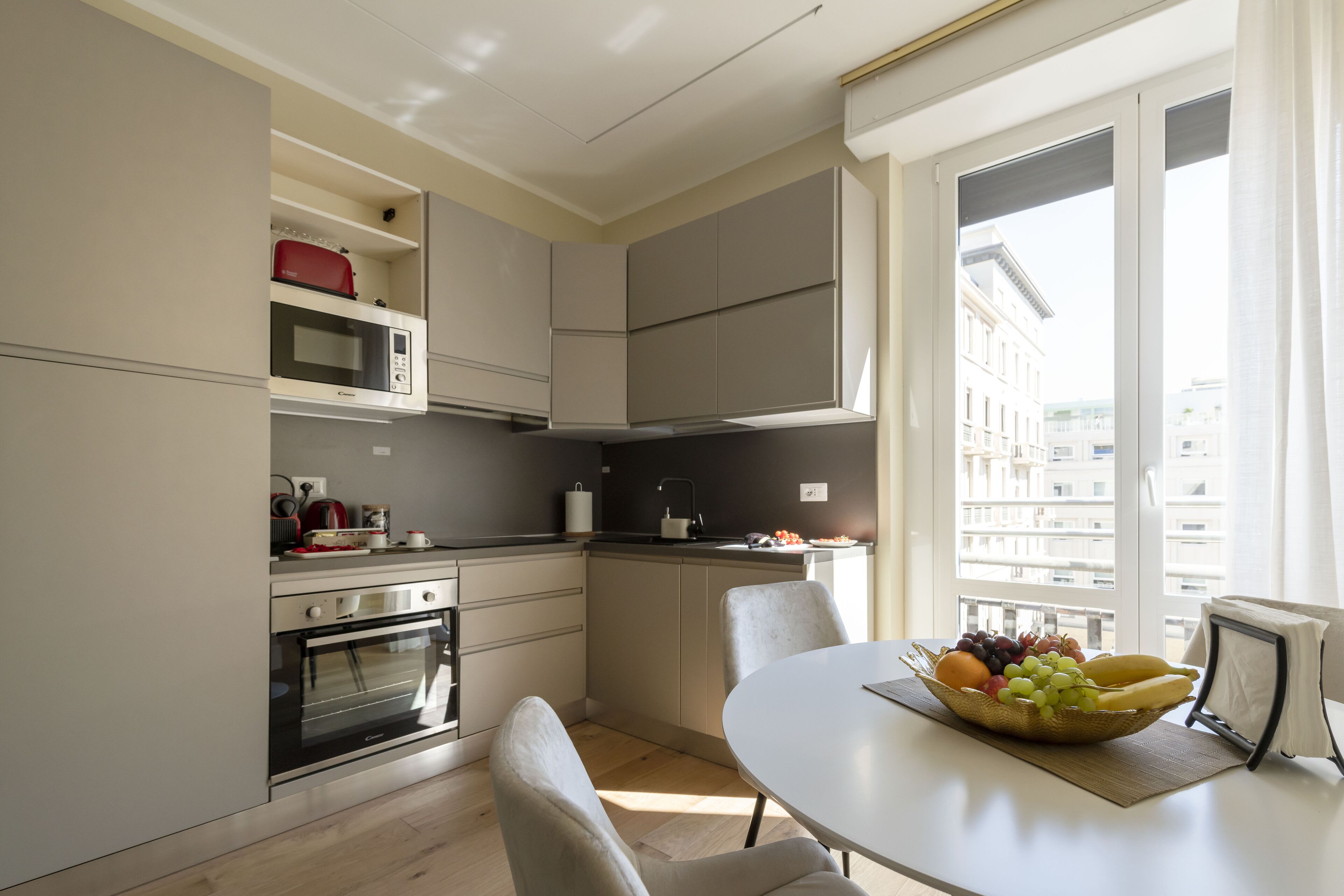 Una cocina moderna con zona de comedor, que incluye horno empotrado, microondas y un amplio ventanal con vistas a la ciudad.