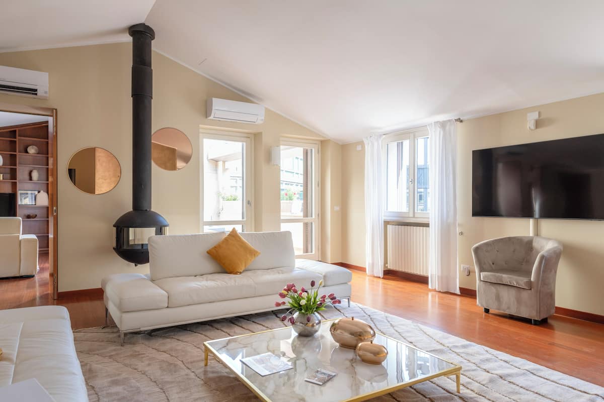 Una sala de estar moderna con un sofá blanco, una mesa de centro de vidrio, una chimenea negra y un televisor en la pared.